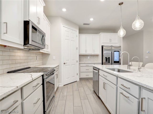 kitchen featuring white cabinets, hanging light fixtures, sink, light stone countertops, and appliances with stainless steel finishes