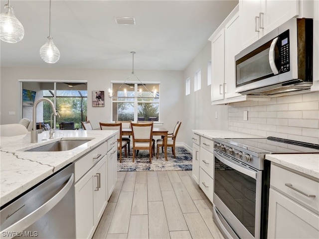 kitchen featuring decorative light fixtures, sink, white cabinetry, and stainless steel appliances