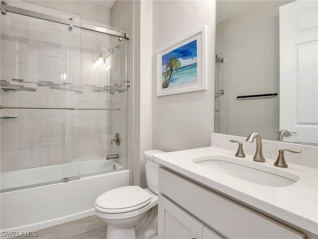 full bathroom with shower / bath combination with glass door, hardwood / wood-style flooring, vanity, and toilet