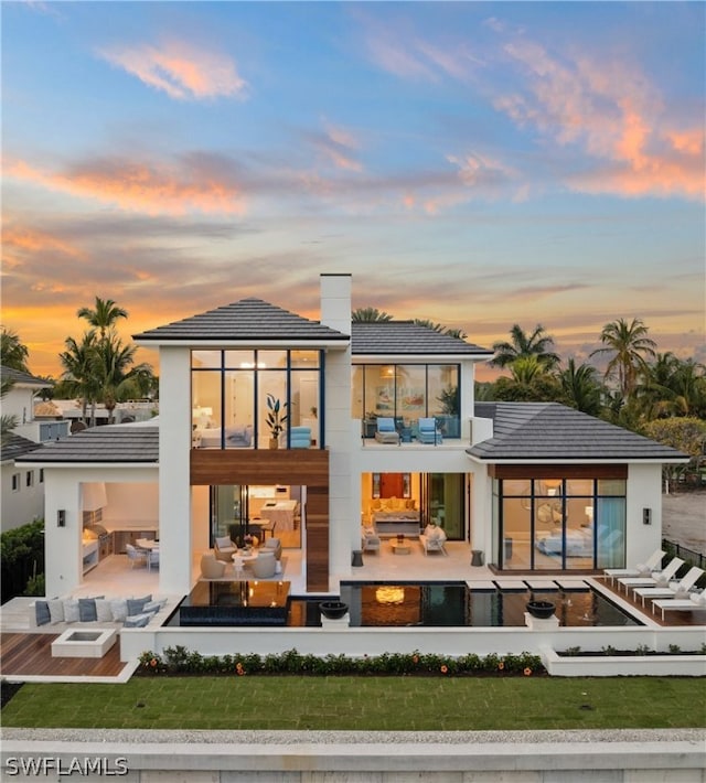 back house at dusk with a yard, an outdoor living space, a balcony, and a patio