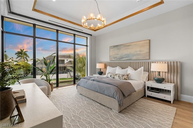 bedroom featuring access to outside, a raised ceiling, an inviting chandelier, and light wood-type flooring