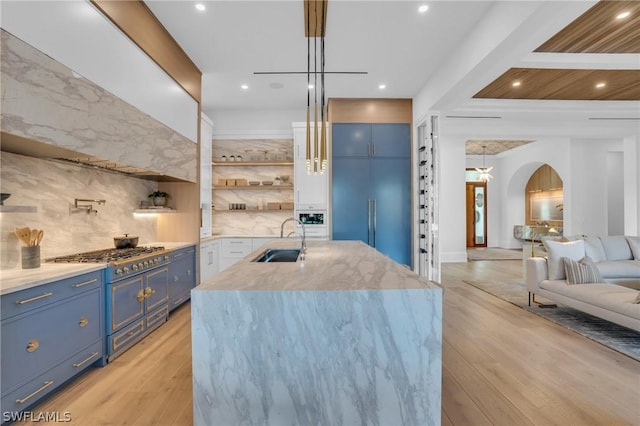 kitchen featuring sink, double oven range, decorative light fixtures, a kitchen island with sink, and light wood-type flooring