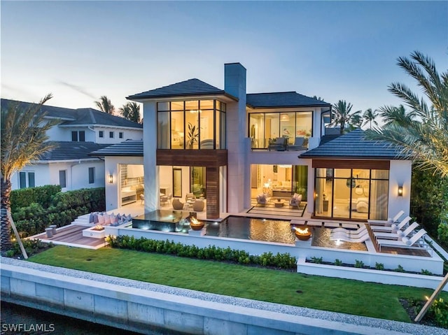 back house at dusk with a lawn, outdoor lounge area, and a patio