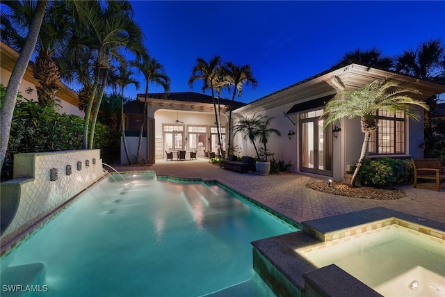 pool at night featuring a patio, french doors, and an in ground hot tub