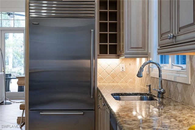 kitchen with backsplash, built in fridge, tile patterned floors, sink, and light stone counters