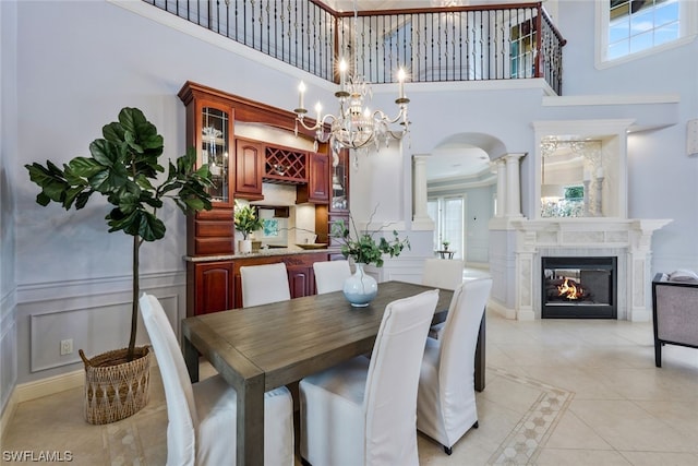 dining room featuring a healthy amount of sunlight, a notable chandelier, ornate columns, and a high ceiling