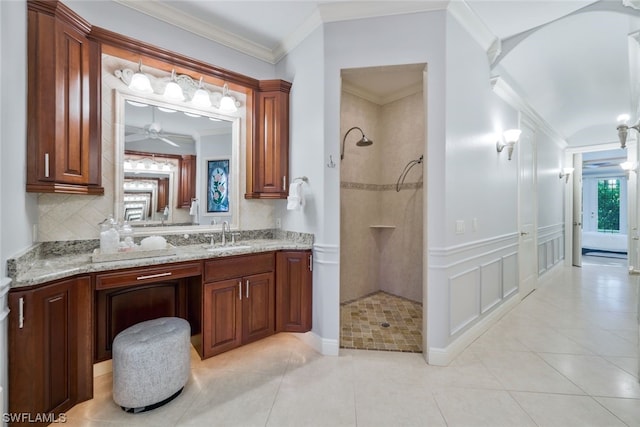 bathroom featuring a tile shower, ceiling fan, crown molding, vanity, and tile floors