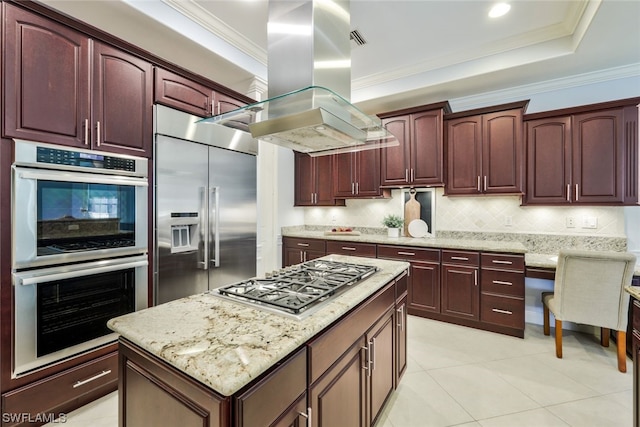 kitchen with backsplash, appliances with stainless steel finishes, a raised ceiling, island exhaust hood, and a kitchen island