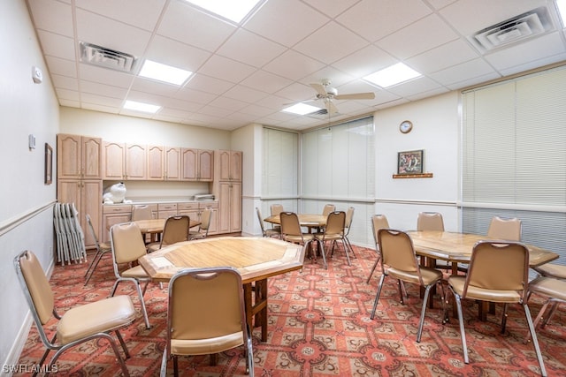 carpeted dining space with ceiling fan and a drop ceiling