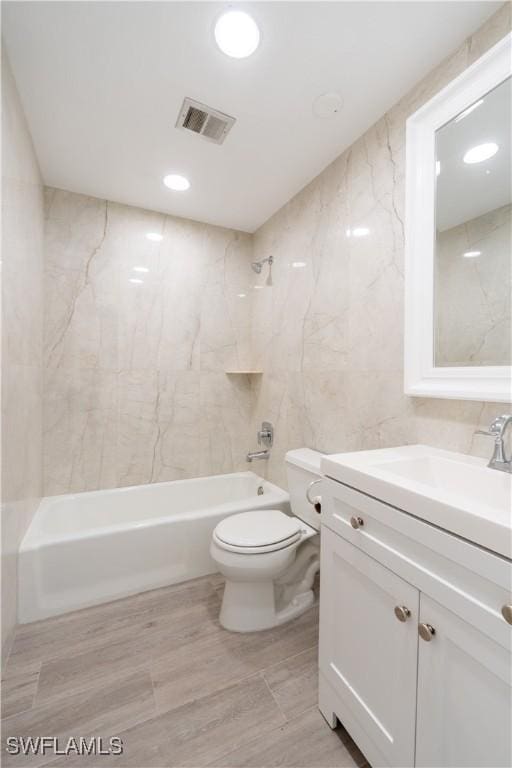 full bathroom featuring tiled shower / bath combo, vanity, tile walls, and toilet