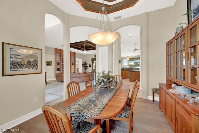 dining area with ceiling fan, a raised ceiling, ornamental molding, a high ceiling, and light wood-type flooring