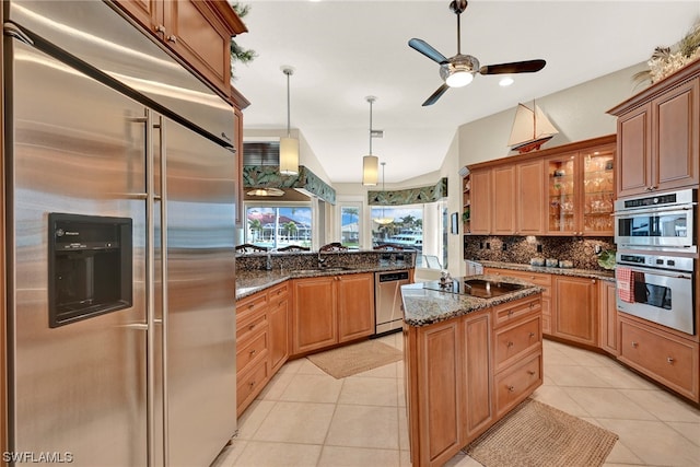 kitchen with ceiling fan, dark stone counters, a center island with sink, stainless steel appliances, and light tile flooring