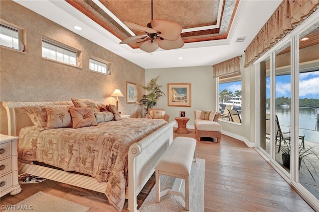 bedroom with access to exterior, ceiling fan, hardwood / wood-style floors, a water view, and a raised ceiling