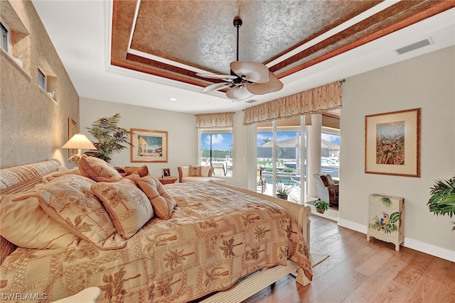 bedroom featuring a tray ceiling, access to exterior, ceiling fan, and light wood-type flooring