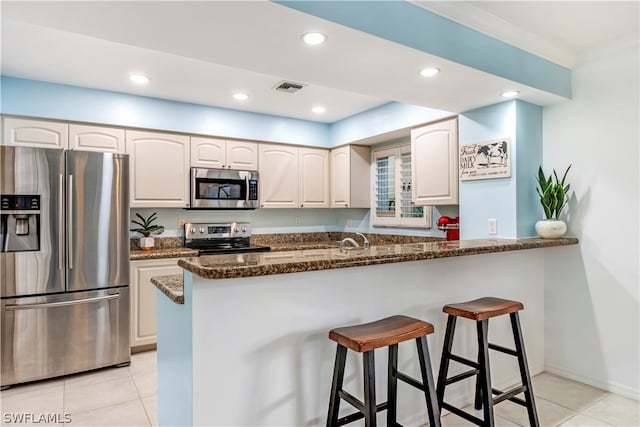 kitchen with a breakfast bar, white cabinets, kitchen peninsula, stainless steel appliances, and dark stone counters