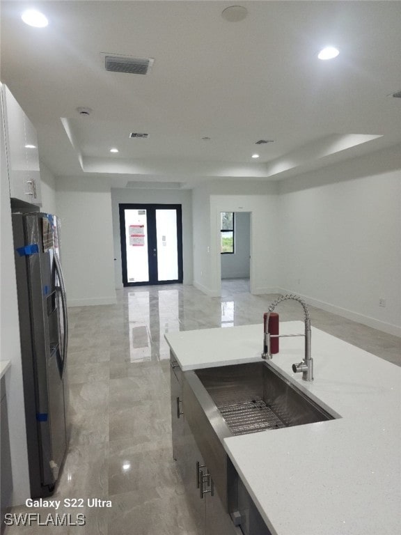 kitchen featuring white cabinetry, sink, french doors, a raised ceiling, and stainless steel fridge