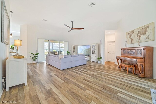 living room with ceiling fan, light wood-type flooring, and a towering ceiling