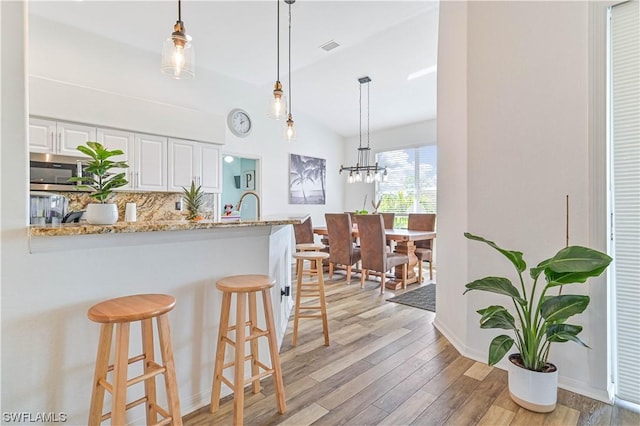 kitchen featuring light stone counters, backsplash, white cabinets, and hanging light fixtures