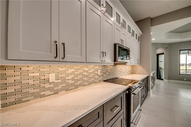 kitchen featuring white cabinetry, stainless steel appliances, light tile floors, light stone counters, and tasteful backsplash