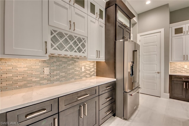 kitchen featuring high end refrigerator, light tile floors, light stone countertops, tasteful backsplash, and white cabinetry