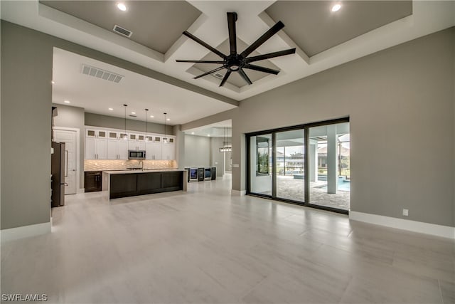 unfurnished living room featuring light tile flooring, a raised ceiling, and ceiling fan with notable chandelier