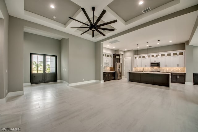 unfurnished living room with a tray ceiling, ceiling fan, light tile floors, and french doors