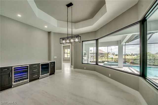 unfurnished dining area featuring a tray ceiling, bar area, light tile floors, and wine cooler