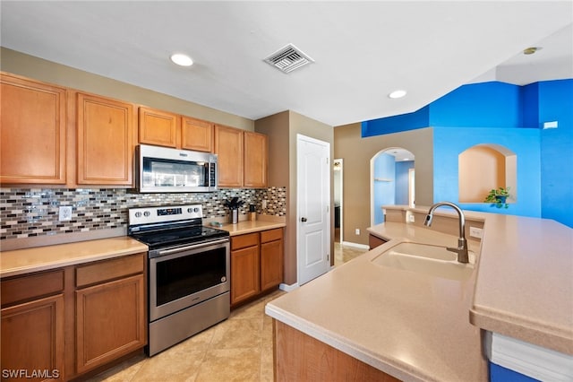 kitchen featuring backsplash, sink, light tile patterned floors, an island with sink, and appliances with stainless steel finishes