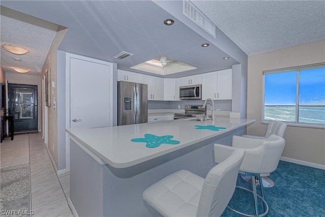 kitchen featuring light tile flooring, a breakfast bar, appliances with stainless steel finishes, white cabinets, and a water view