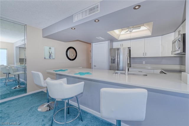 kitchen featuring light carpet, kitchen peninsula, stainless steel appliances, and white cabinetry