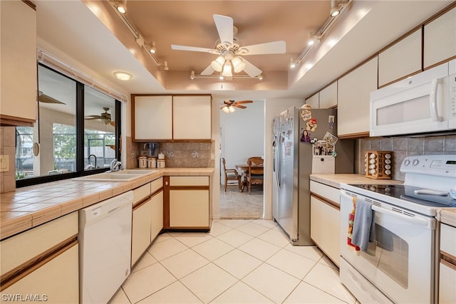 kitchen with backsplash, white appliances, a tray ceiling, sink, and tile counters