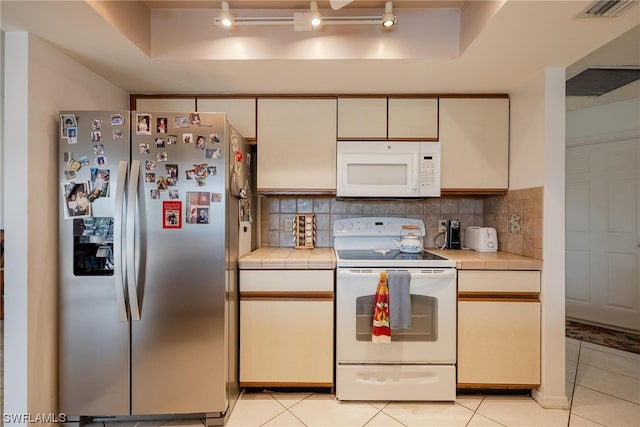 kitchen featuring a tray ceiling, tasteful backsplash, light tile patterned flooring, and white appliances