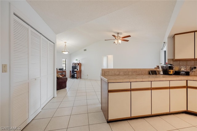 kitchen with ceiling fan, backsplash, vaulted ceiling, cream cabinetry, and light tile patterned floors