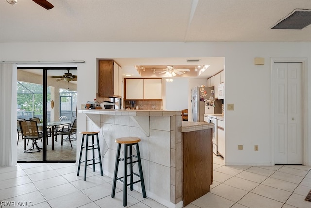 kitchen with light tile patterned floors, tasteful backsplash, white appliances, a breakfast bar, and white cabinets