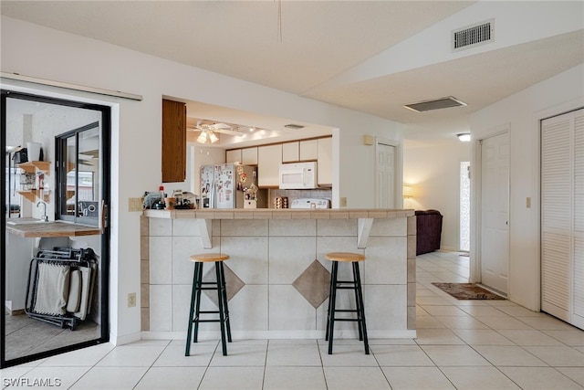 kitchen with a breakfast bar, stainless steel refrigerator with ice dispenser, tile countertops, and vaulted ceiling