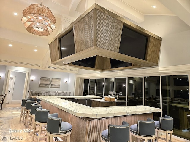 bar with an inviting chandelier, wall chimney range hood, and high vaulted ceiling