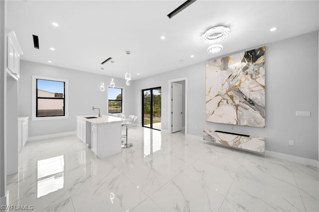 interior space with decorative light fixtures, white cabinetry, a kitchen breakfast bar, an island with sink, and light tile floors