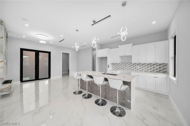 kitchen featuring an island with sink, light tile floors, hanging light fixtures, tasteful backsplash, and white cabinetry