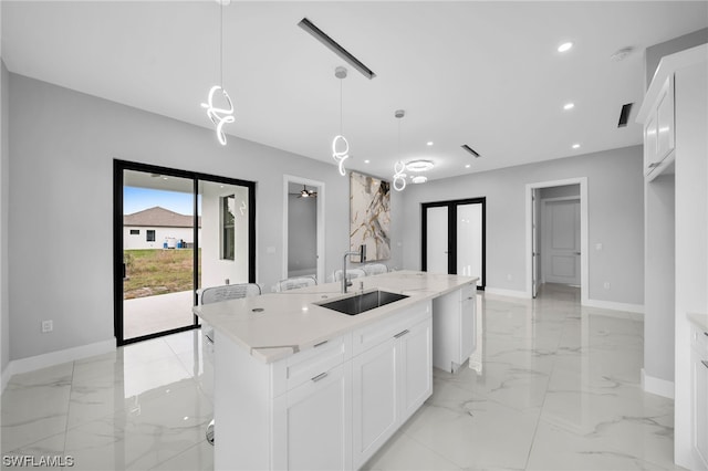 kitchen featuring pendant lighting, light tile floors, white cabinets, a kitchen island with sink, and sink