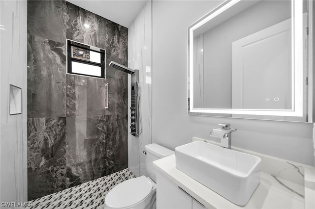 bathroom with toilet, a tile shower, and vanity