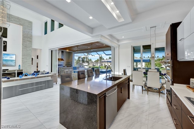 kitchen featuring sink, dark brown cabinets, a center island with sink, dishwasher, and a notable chandelier