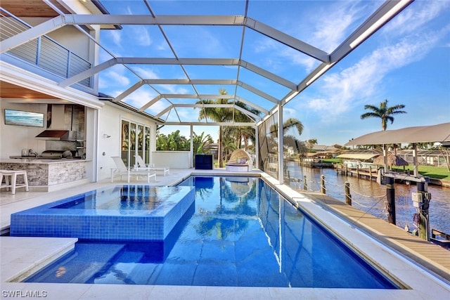 view of swimming pool featuring exterior kitchen, a water view, glass enclosure, a patio area, and an in ground hot tub