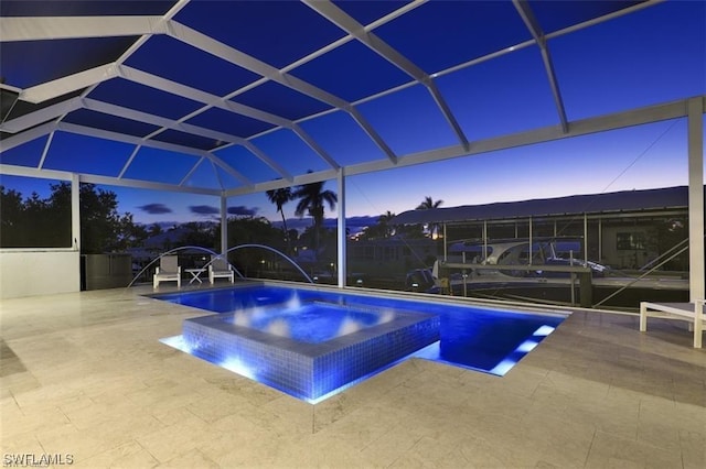 pool at dusk featuring an in ground hot tub, pool water feature, glass enclosure, and a patio area