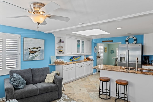 kitchen featuring dark stone counters, a skylight, light tile flooring, stainless steel refrigerator with ice dispenser, and white cabinetry