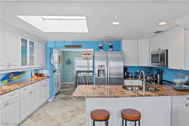 kitchen featuring stainless steel appliances, light tile floors, a skylight, white cabinets, and light stone counters