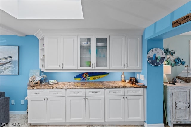 kitchen with light tile floors, a skylight, white cabinets, and light stone countertops