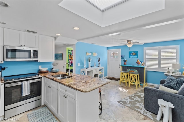 kitchen featuring stainless steel appliances, light tile flooring, ceiling fan, white cabinetry, and sink