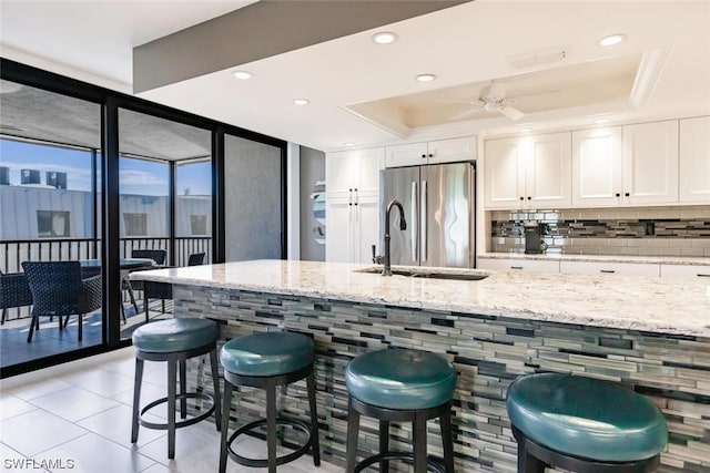 kitchen with white cabinets, ceiling fan, a kitchen bar, and stainless steel refrigerator