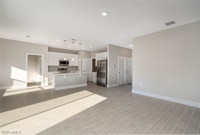 kitchen with hanging light fixtures, a kitchen island with sink, stainless steel appliances, light tile floors, and white cabinets