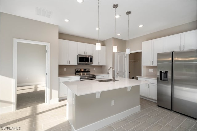 kitchen featuring sink, hanging light fixtures, appliances with stainless steel finishes, a center island with sink, and white cabinetry